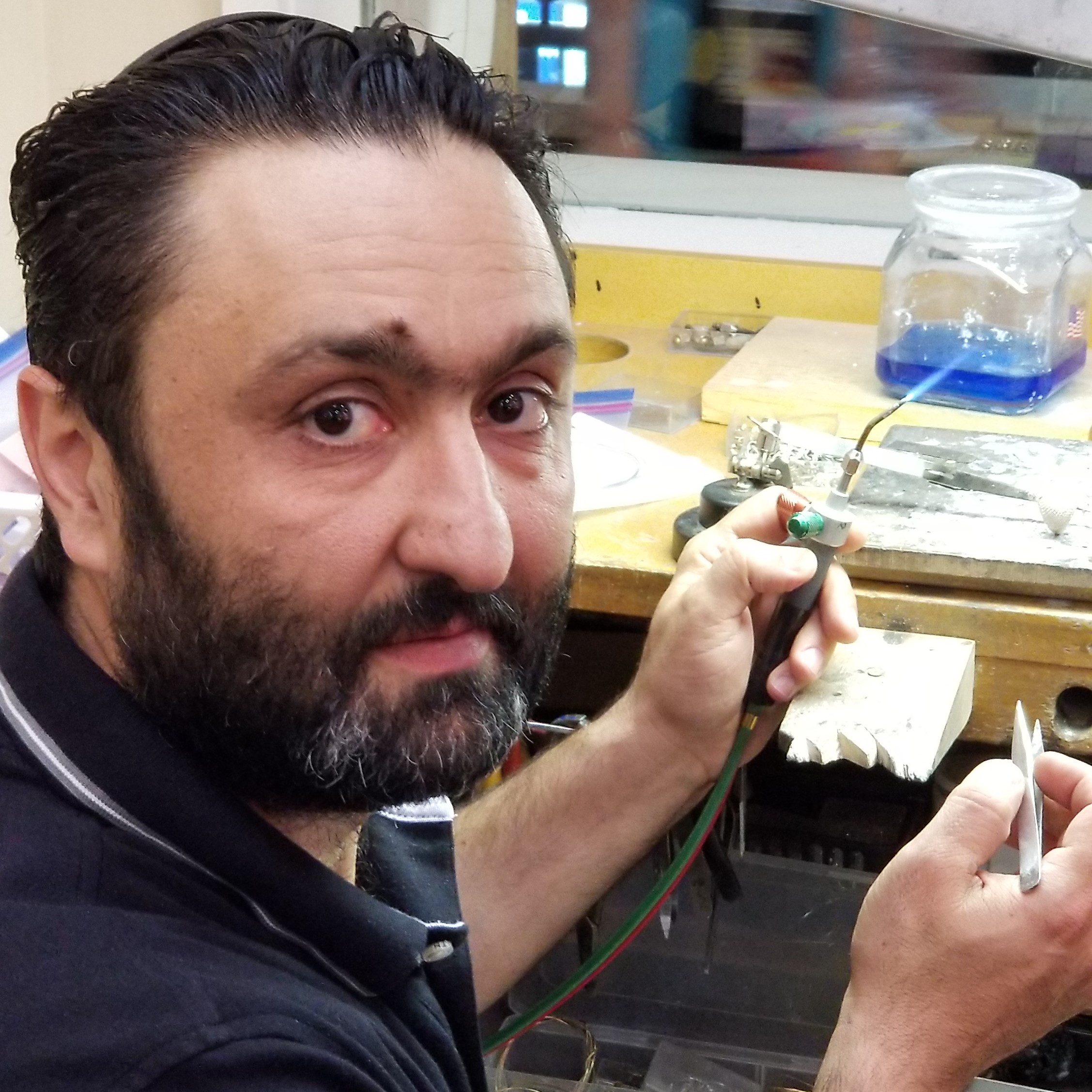 Michael Gadelov holds a jewelry torch and a pair of tweezers to complete a job at his Jewelers Bench