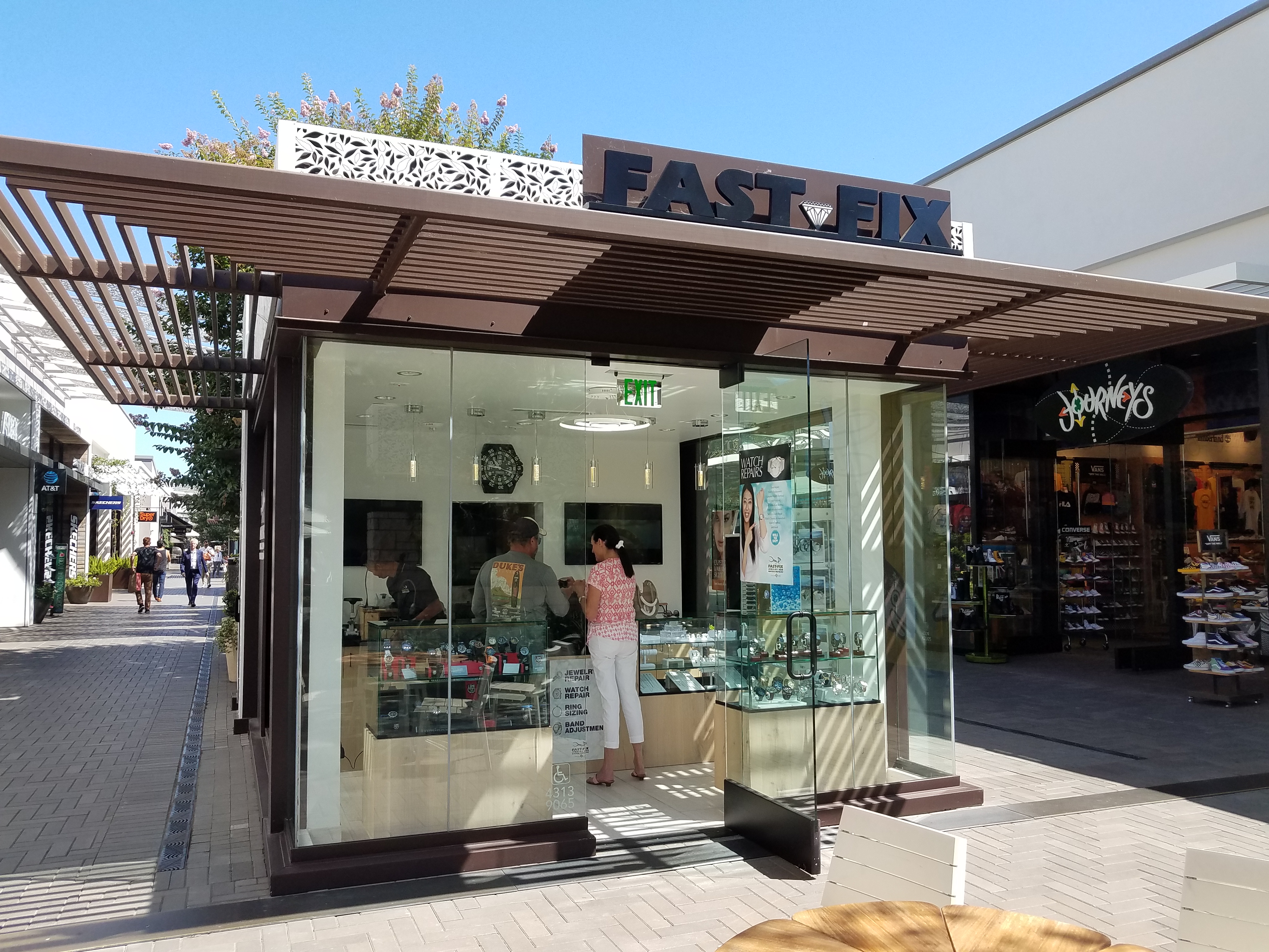 Fast-Fix Jewelry and Watch Repairs kiosk. Picture of its exterior showing a glass front with wood frame and clear view of the front desk and jewelry display.